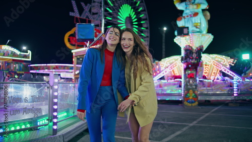 Happy girls walking illuminated amusement park. Smiling best friends enjoying