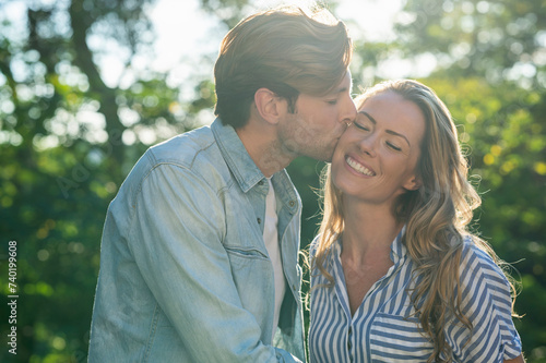 Billede på lærred Adult man kissing girlfriend on the cheek while standing outdoors