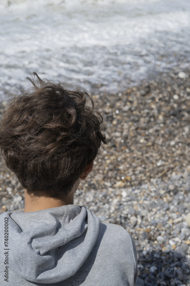 Fototapeta premium Rear view of young person's head looking at seaside waves in Normandie