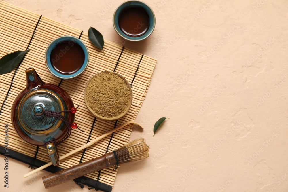 Fototapeta premium Bamboo mat with cups of matcha tea, teapot, chashaku and chasen on beige background