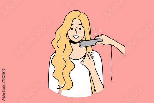 Woman at hairdresser appointment using hair straightener to straighten curls before party or date. Happy blonde girl visits hairdresser or stylist who helps change image and become more beautiful