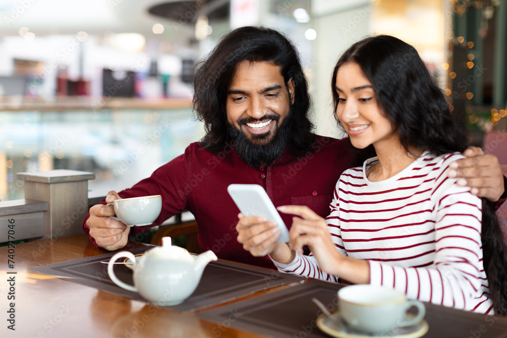 Cheerful loving indian couple have date at cafe, using phone Cheerful loving indian couple have date at cafe, using phone