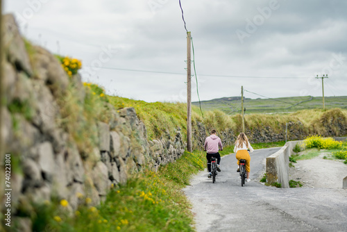 Tourists riding electric bikes on Inishmore, the largest of the Aran Islands in Galway Bay, Ireland. Renting a bicycle is one of the most popular way to get around Inis Mor.