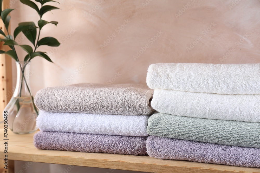 Stacked soft towels and green leaves on wooden shelf indoors Stacked soft towels and green leaves on wooden shelf indoors