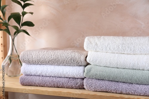 Stacked soft towels and green leaves on wooden shelf indoors