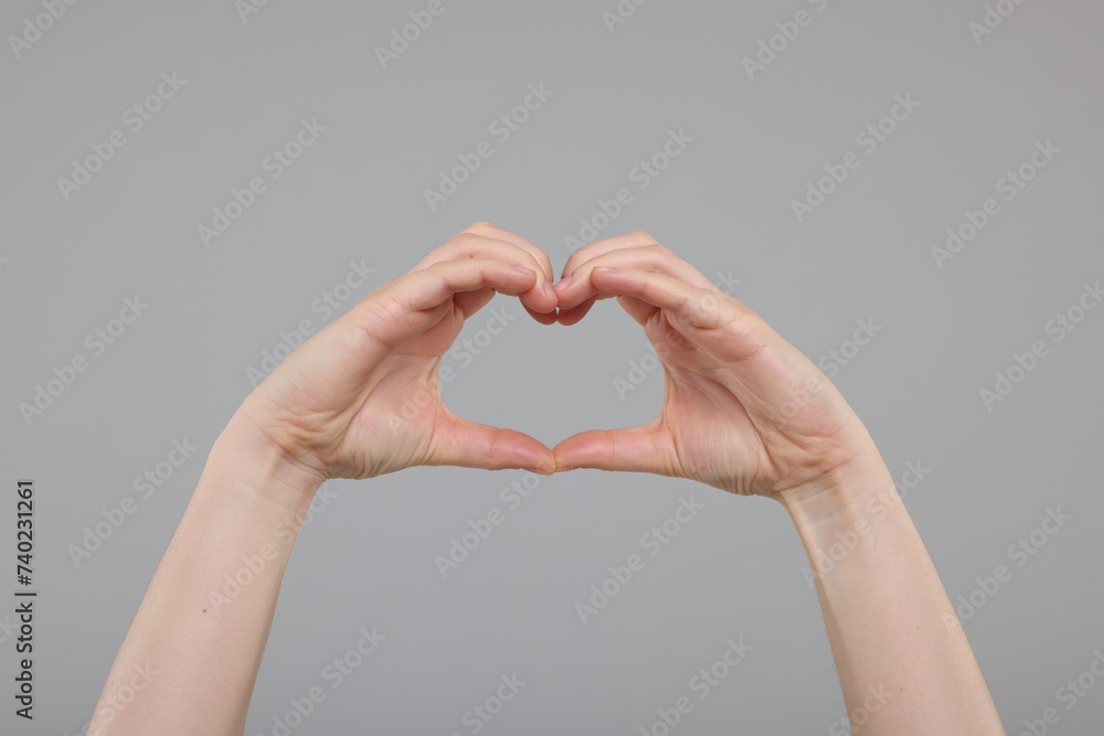 Obraz premium Woman showing heart gesture with hands on grey background, closeup