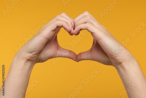 Man showing heart gesture with hands on golden background, closeup photo