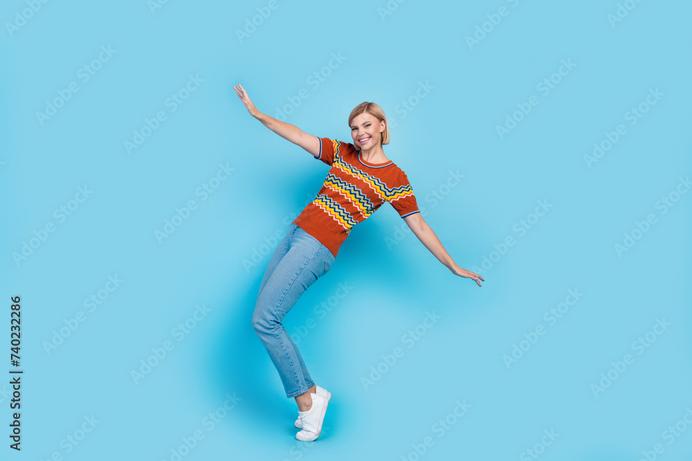 Full size photo of funny positive gorgeous woman dressed knit t-shirt denim pants dancing on tiptoes isolated on blue color background