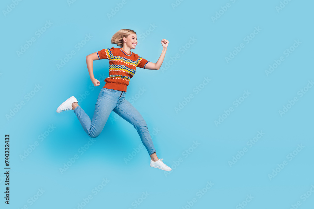 Full size photo of fast active woman dressed knit t-shirt clenching fists run shopping to empty space isolated on blue color background Full size photo of fast active woman dressed knit t-shirt clenching fists run shopping to empty space isolated on blue color background