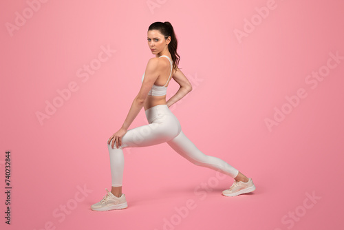 Fototapeta Naklejka Na Ścianę i Meble -  Focused and toned young woman in a white sports bra and leggings performing a stretching