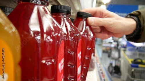 Close-up of many berry juice bottles standing in a row in a supermarket and a male buyer's hand taking one