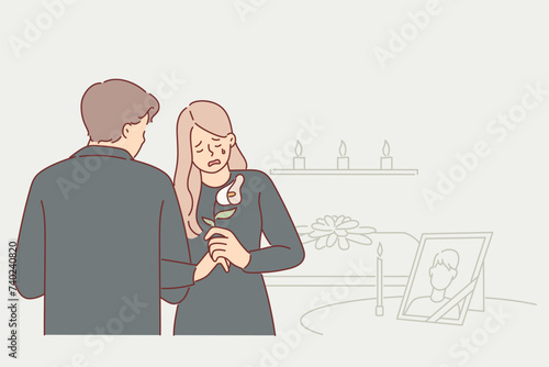 Widow woman cries at funeral standing near table with portrait of deceased husband at mourning event