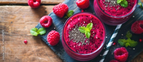 Two glasses of forest berry smoothie with raspberries and mint are placed on a rustic wooden table.