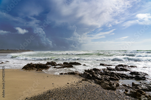 Baie d'Audierne en Bretagne : sable, rochers, océan agité aux reflets émeraude sous un ciel aux nuages contrastés.
