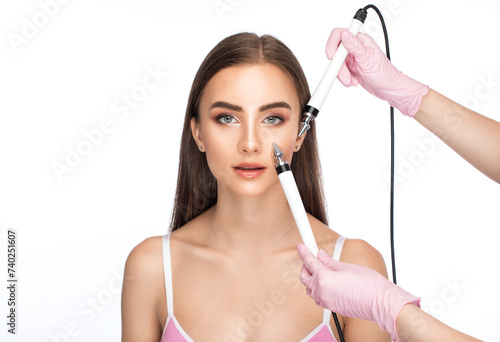A doctor cosmetologist makes a microcurrent facial therapy to a young woman with a device in a beauty wellness salon. Cosmetology and professional skin care.