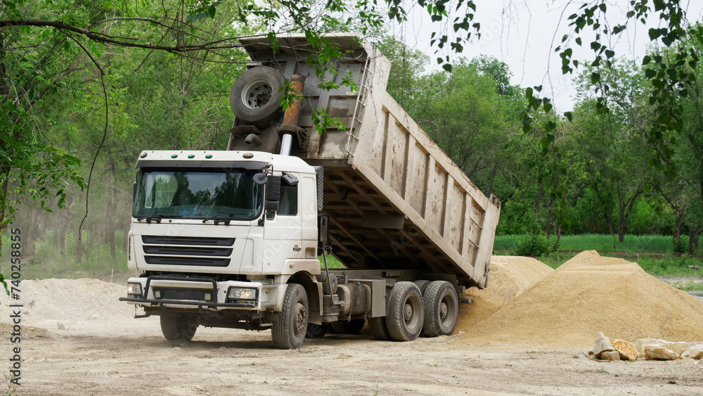 A heavy service truck - dump truck unloads sand among trees, in a forest or park. Environmental problems. Photo A heavy service truck - dump truck unloads sand among trees, in a forest or park. Environmental problems. Photo