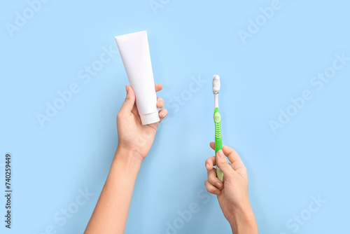 Female hands with toothbrush and toothpaste on blue background.