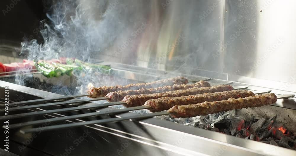 Adana kebab barbecue on charcoal grill in a restaurant. Smoke rising over traditional Turkish kebab, tomatoes and peppers grilled on skewers. Close-up Adana kebab barbecue on charcoal grill in a restaurant. Smoke rising over traditional Turkish kebab, tomatoes and peppers grilled on skewers. Close-up