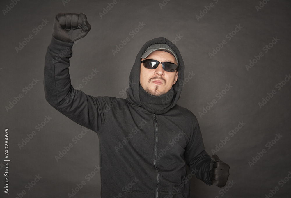 Serious Man in the black hoody with hood wearing sunglasses with fist Serious Man in the black hoody with hood wearing sunglasses with fist