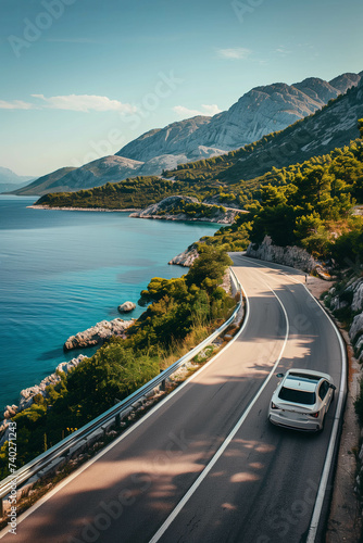 Drone view of a car driving on a road that cuts through mountains and sea.