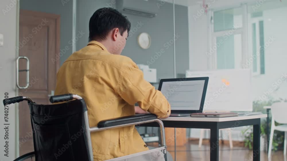 Tilt up shot of male programmer with disability fixing bugs in script sitting at office desk back view Tilt up shot of male programmer with disability fixing bugs in script sitting at office desk back view