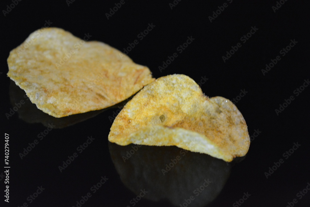 Food, product, potato pieces, potato chips arranged on black glossy background.