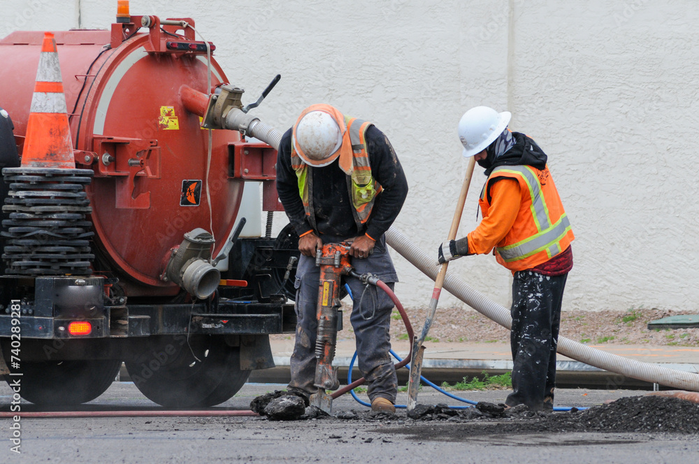 Construction workers using power and hand tools to break street pavement for road improvement