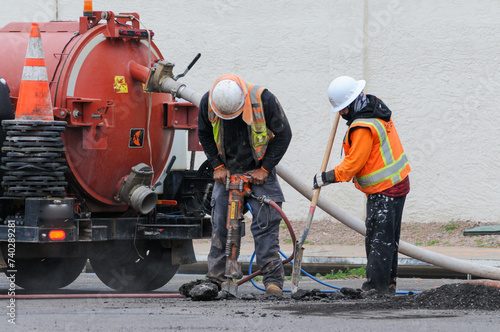 Construction workers using power and hand tools to break street pavement for road improvement