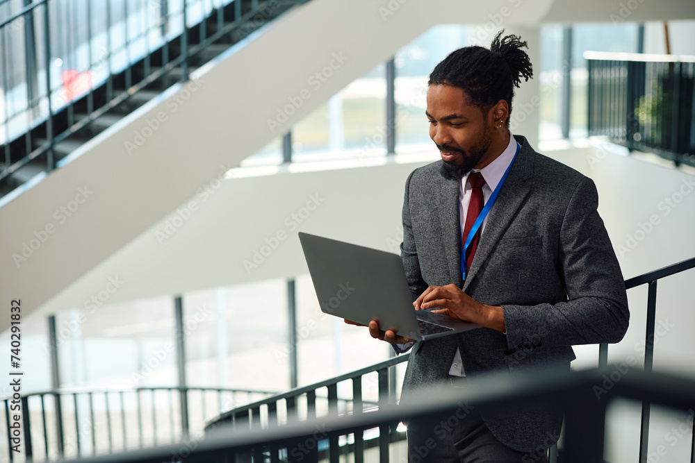 Happy black businessman working on laptop in hallway. Happy black businessman working on laptop in hallway.