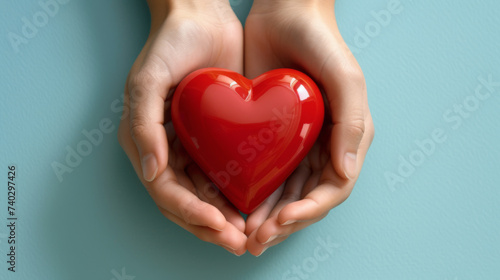 two hands gently holding a glossy red heart against a soft blue background, symbolizing care, love, and health.