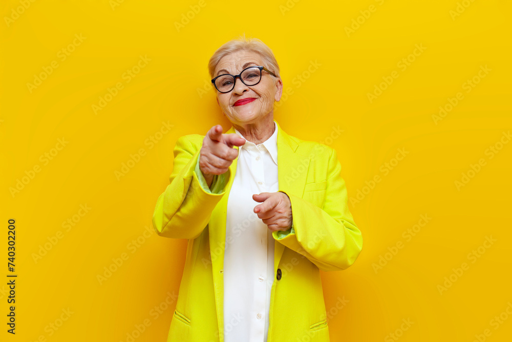 old businesswoman in glasses and formal wear points with hands at camera and smiles on yellow isolated background, elderly pensioner grandmother in blazer points with hands forward at camera old businesswoman in glasses and formal wear points with hands at camera and smiles on yellow isolated background, elderly pensioner grandmother in blazer points with hands forward at camera