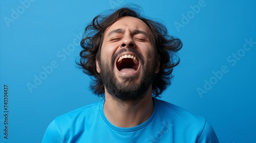 Joyful man laughing with eyes closed against blue background