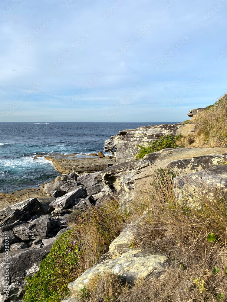 The coast of the sea. Mountains cliff in the ocean. View of the rocky coast of island, Australia. Waves curling on the rocky shore.