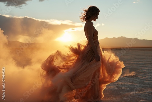 A woman in a flowing orange gown poses amidst a dramatic, ethereal mist