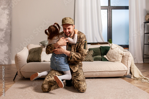 happy Ukrainian army soldier in camouflage uniform returned home and meets his daughter, the child runs to his military dad and hugs the veteran at home photo