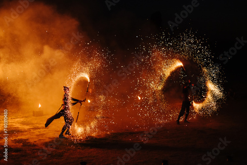 People dance a passionate dance with a fiery spinning wheel in hand. Tribal dancer. Fire show. Spin fire around a swing on the beach in a full moon. The fire shows many sparks at night