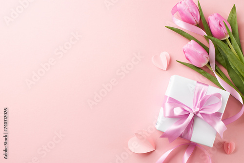 Tokens of affection: celebrating her with elegance. Top view shot of white gift box tied with pink ribbon, pink tulips on pink background with space for custom dedications or brand messaging © Goncharuk film