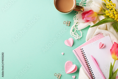 International Women's Day: celebration of femininity and respect. Top view of cup of coffee, pink notebook, pen, tulips, mimosa, heart-shaped decor on teal background with space for heartfelt messages photo