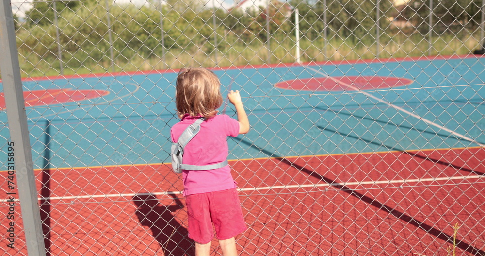 A child with a broken arm outdoors near a playground fence. The concept of health, injuries related to sports.