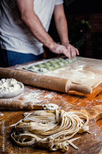 A chef is at work making two different types of handmade pasta: fettuccine and ravioli.