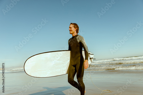 Happy handsome male surfer in wetsuit with his surfboard entering out of sea after surfing