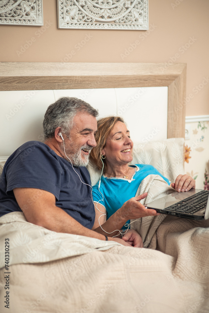 vertical portrait Digital Connection in Golden Years: Senior Couple Enjoying Entertainment in Bed vertical portrait Digital Connection in Golden Years: Senior Couple Enjoying Entertainment in Bed