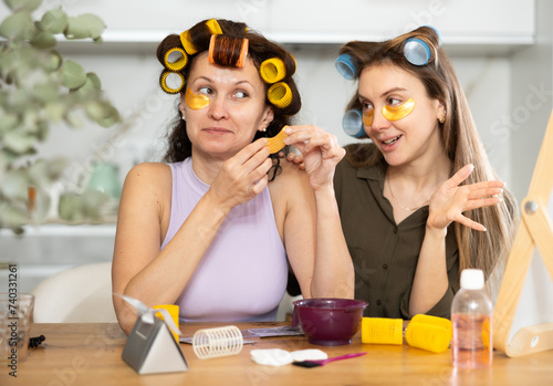 Adult woman and young woman curling hair with curlers and using eye patches photo