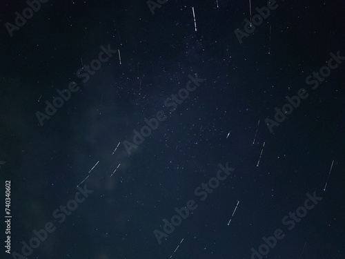 Starry night sky in village. A black-gray night sky in which white spots of distant stars are visible. Gray clouds float across the sky, covering some of the stars. Stars can be seen across the sky. © Andrew_Swarga