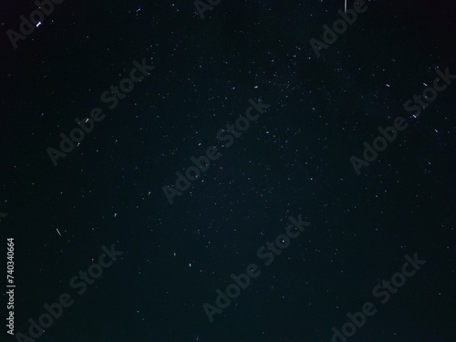 Starry night sky in village. A black-gray night sky in which white spots of distant stars are visible. Gray clouds float across the sky, covering some of the stars. Stars can be seen across the sky.