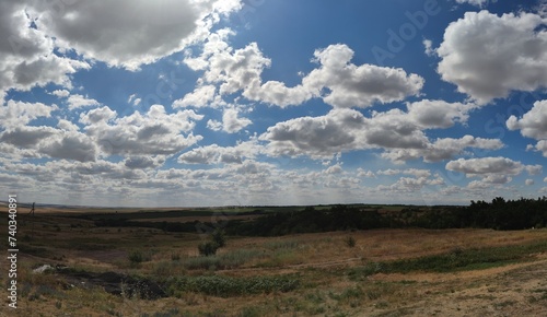 Countryside from the hill. Under a bright sky with white cirrus clouds, a rural landscape with wide fields, hills and forest plantations is visible. Steppes of the Caucasian Upland.