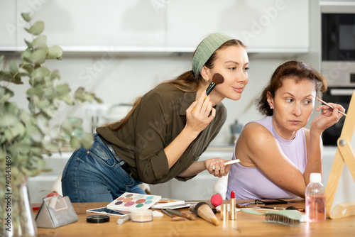 Two adult besties doing everyday makeup together in front of vanity mirror in well-lit cozy room  perfecting their look with care and precision