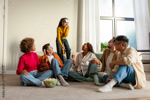 multiracial group of young friends playing charades drinking beer and having fun at home