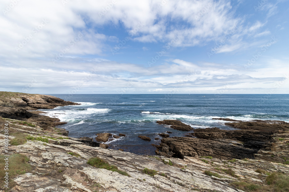 a picturesque view of a rocky coastline with layered formations, under a partly cloudy sky, exuding serene beauty