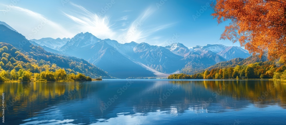 A stunning lake, bordered by majestic mountains and adorned with vibrant trees in the foreground, on a beautiful autumn day.